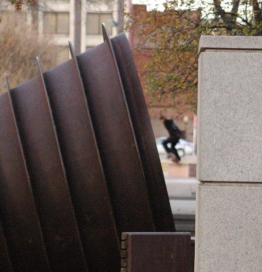 A distant, out of focus skateboarder jumps across the street from The Harrow.